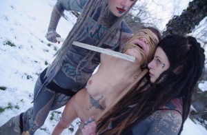 Heavily tatted girls torture a naked girl that is tied to a tree in the snow