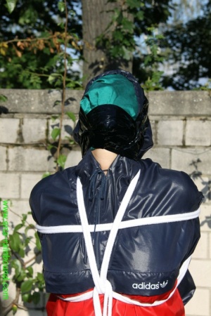Submissive woman Sandra is tied up while wearing a raincoat in a sunny yard
