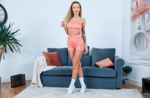 Young blonde Elena Lux strips to white socks and sneakers on a loveseat