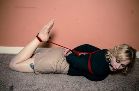 Clothed woman with blonde hair sports a ball gag in mouth while hogtied 83836194